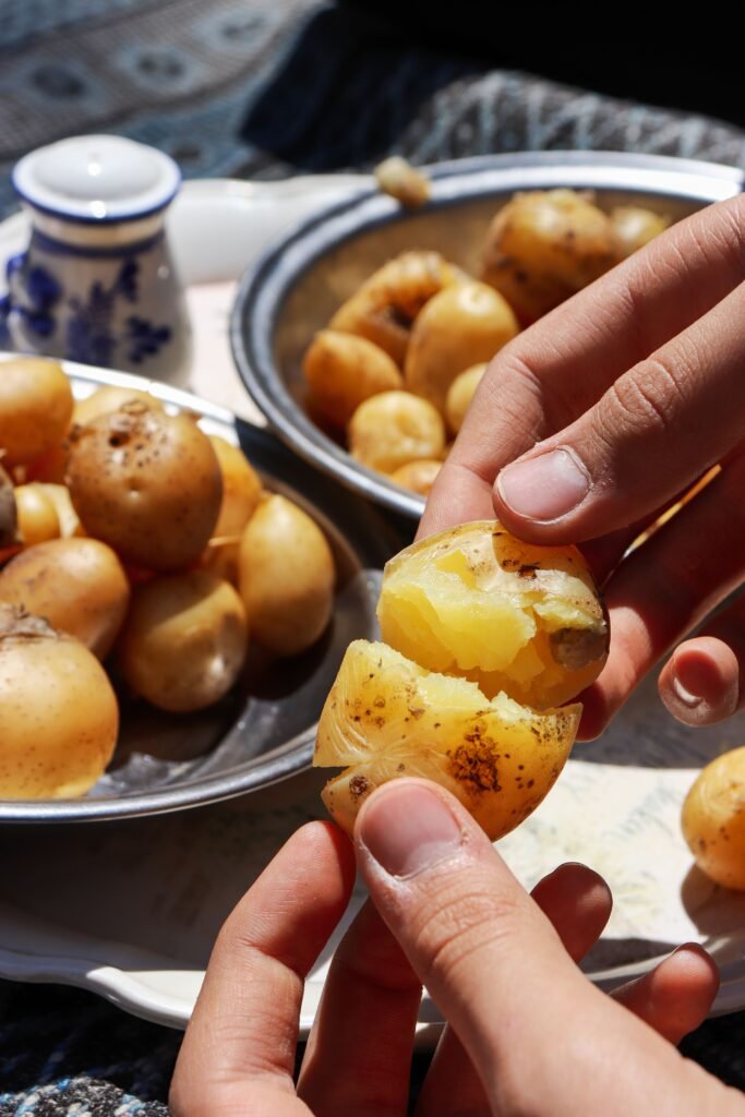 Mãos partindo uma batata cozida ao meio, com tigelas de batatas cozidas ao fundo