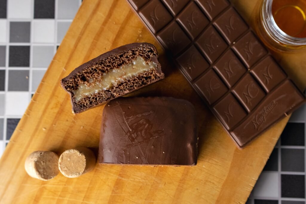Chocolate em barra e bombons recheados cortados ao meio sobre tábua de madeira