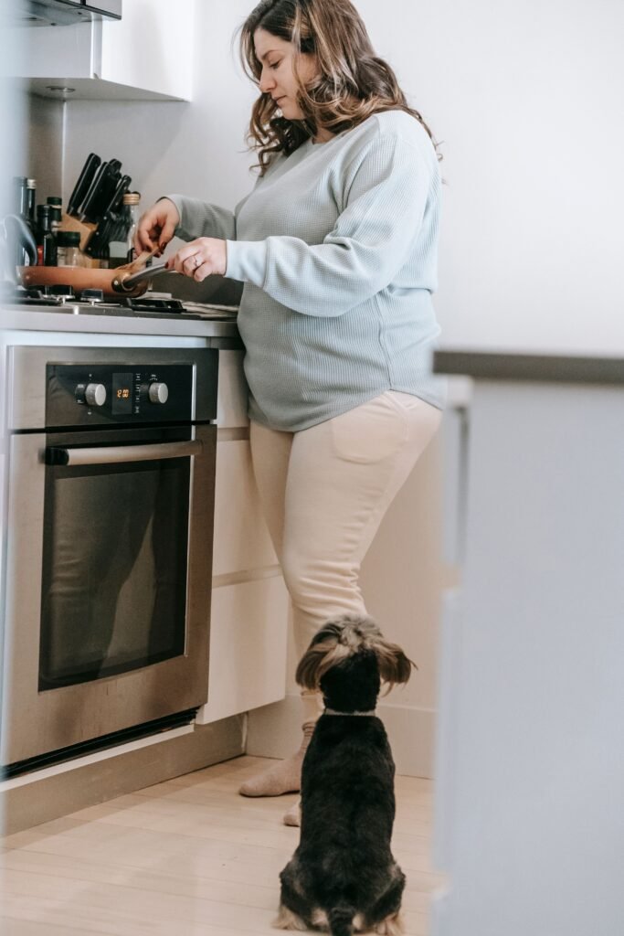 cachorro esperando ao lado de mulher preparando refeição na cozinha