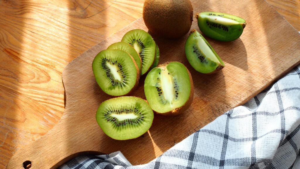 Kiwis inteiros e fatiados dispostos sobre uma tábua de madeira em uma cozinha iluminada